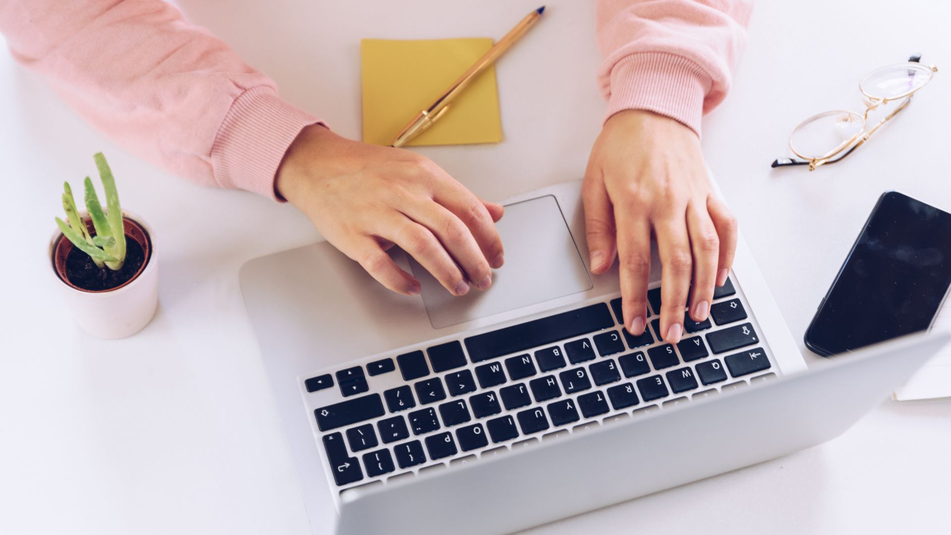 Hands typing on a laptop standing on a desk.