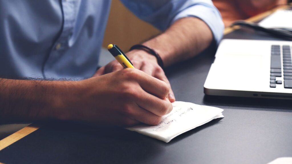 Person writing new topic ideas in notepad.