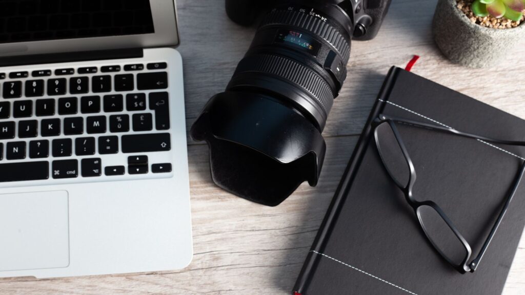 Desk of a content creator with a laptop, camera, and notebook.