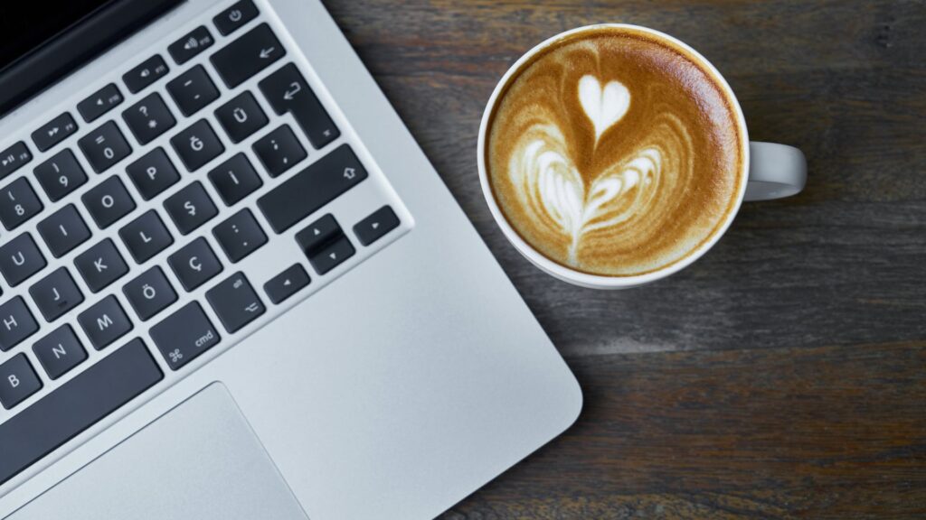 Laptop keyboard with a cup of coffee next to it.