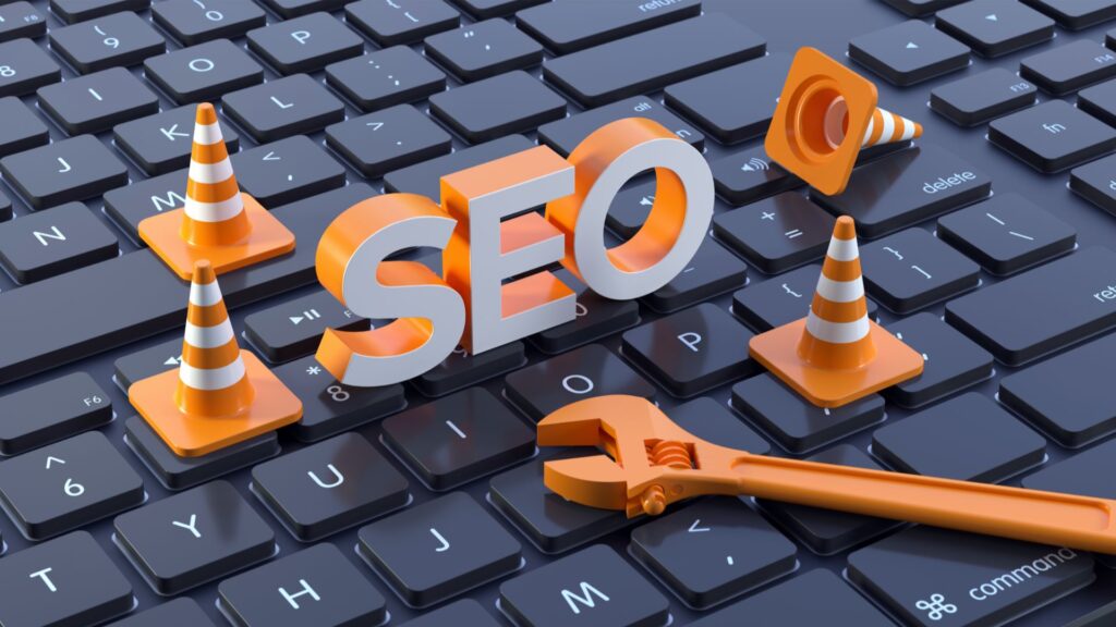 The word "SEO" on a laptop keyboard next to tools and cones.