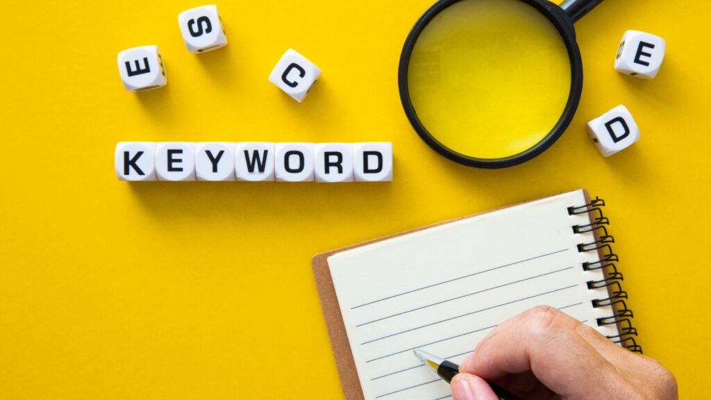 Dices forming the word "keyword", a notepad, and a magnifying glass on a yellow background.