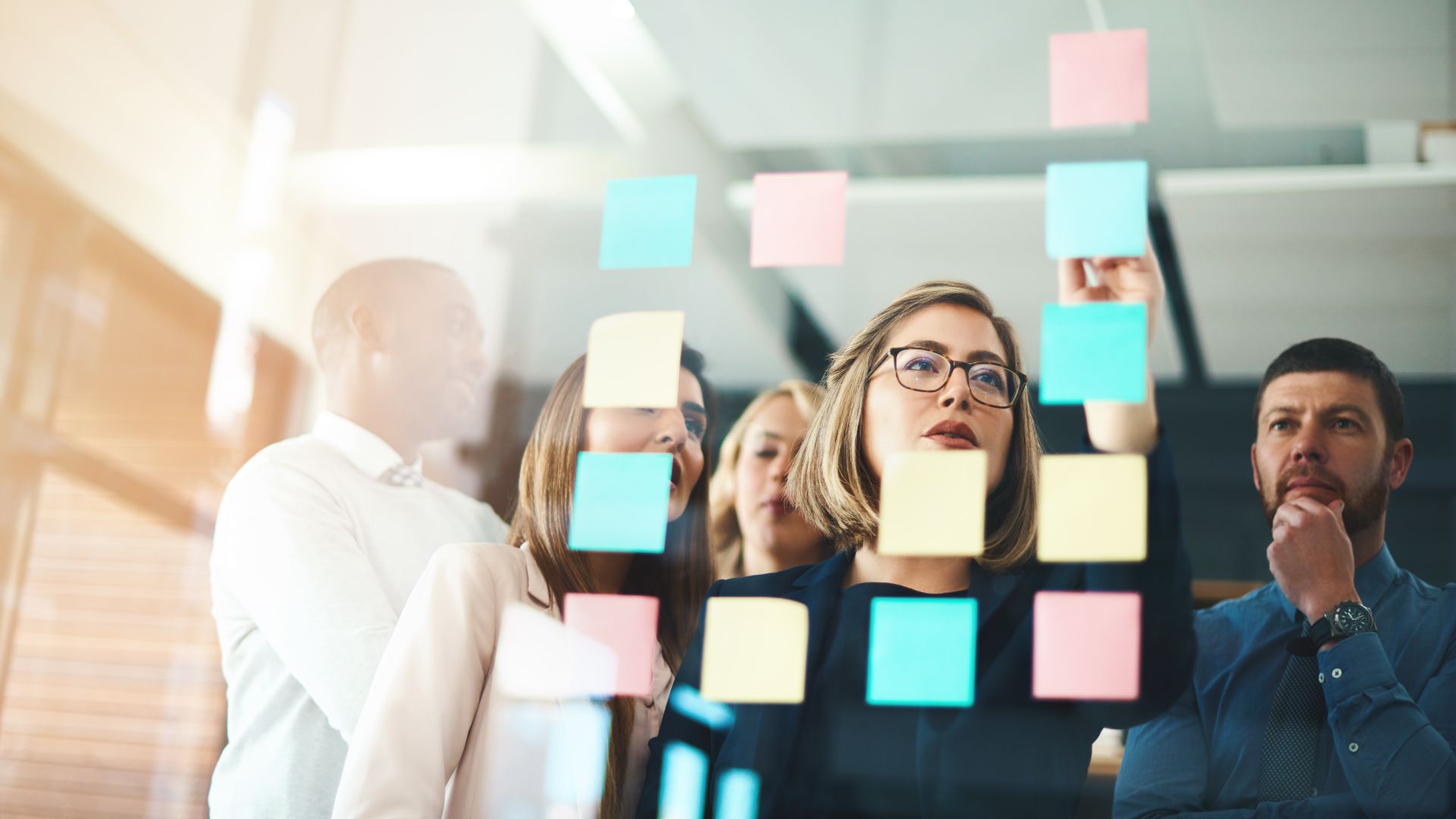 Persons looking at post it notes on a glass wall containing content marketing trends.