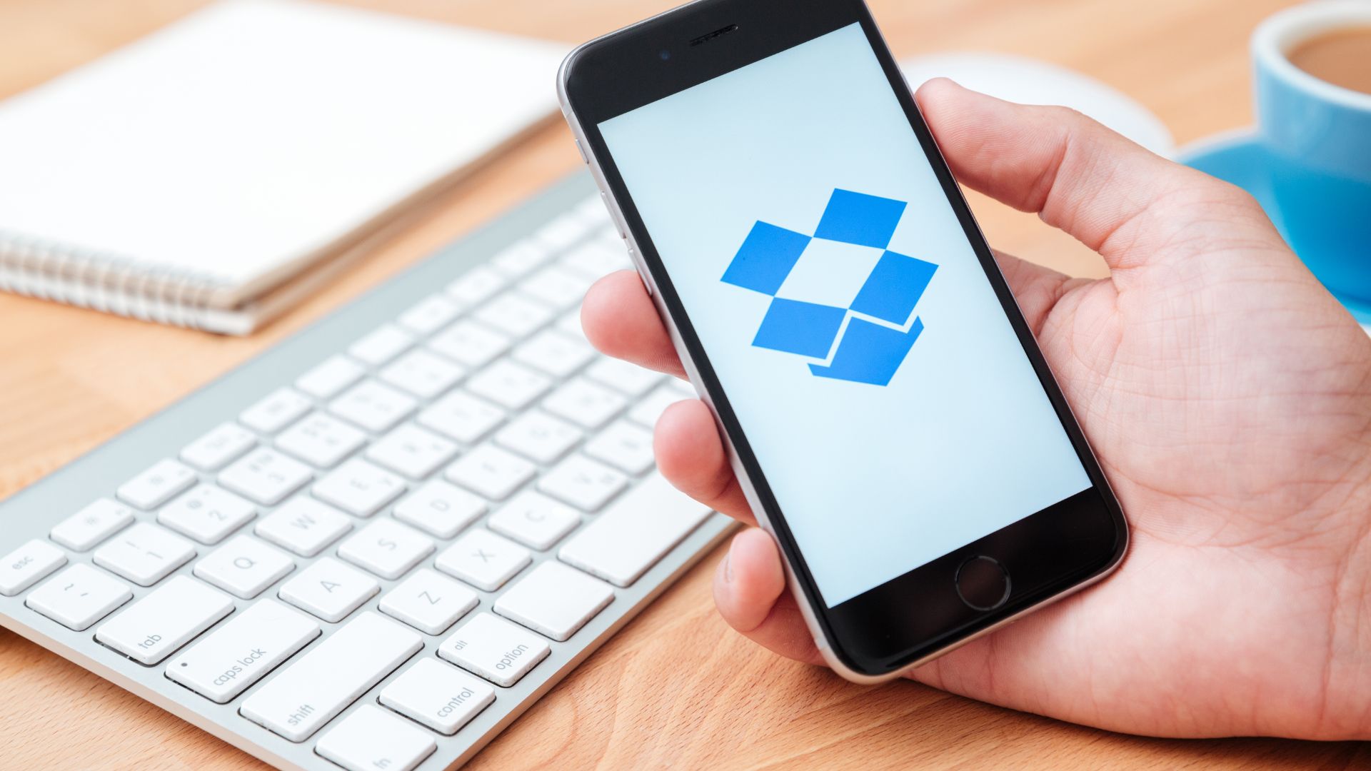 Dropbox user holding smartphone in front of laptop keyboard.