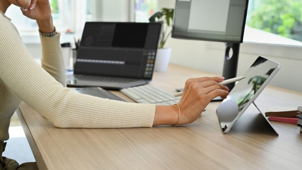 Person sitting by desk with laptop, tablet and computer screen on it.