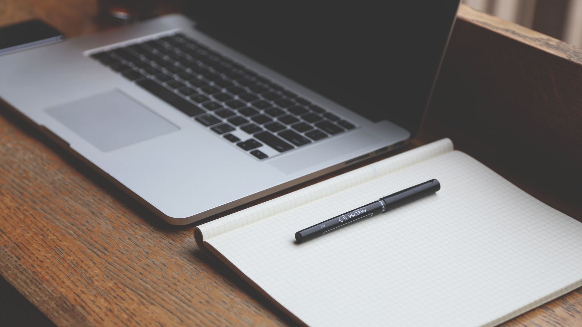 Laptop on desk next to notepad and pen.