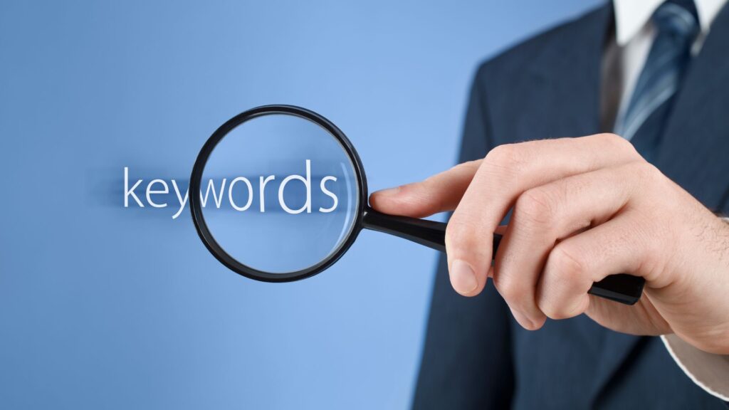 Man in a suit holding a magnifying glass over the word "keywords" on a blue background.