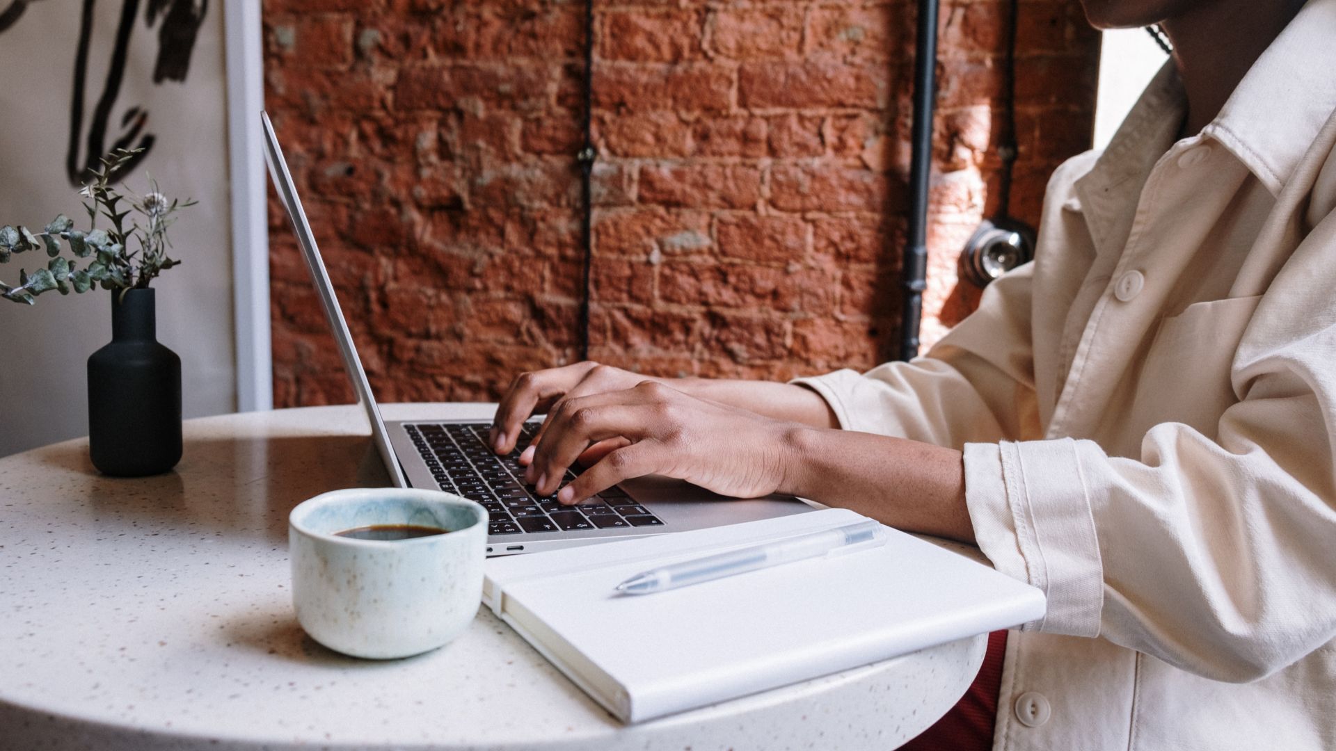 Person sitting by table with a laptop and a cup of coffee on it.