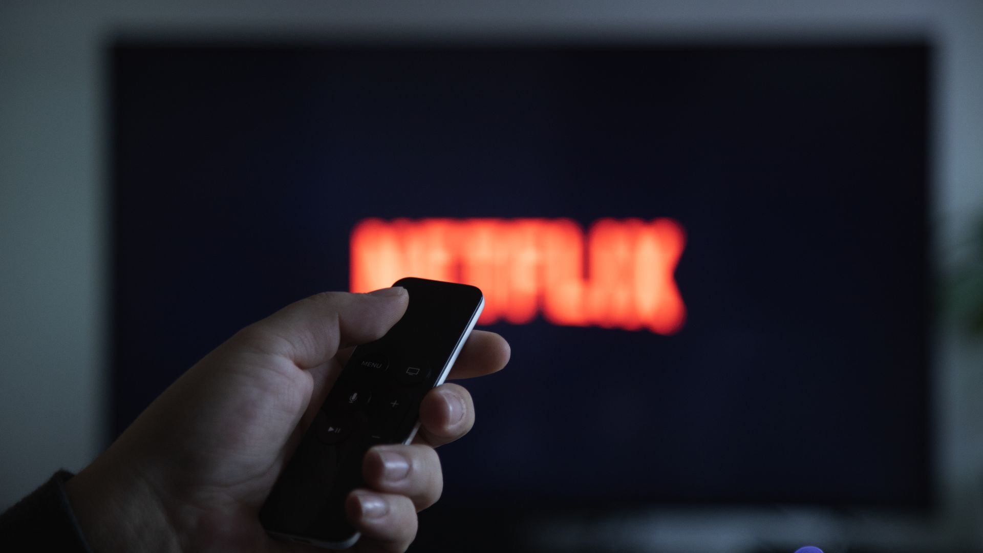 Hand pointing remote at tv with Netflix logo on the screen.