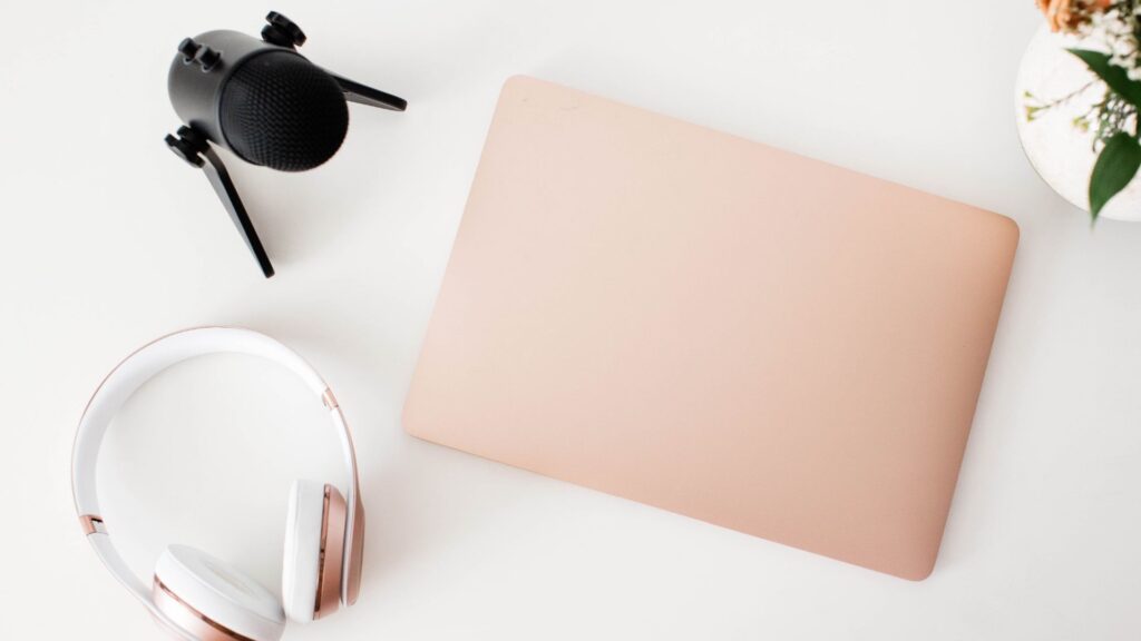 Desk with podcast microphone, laptop and headphones on it.