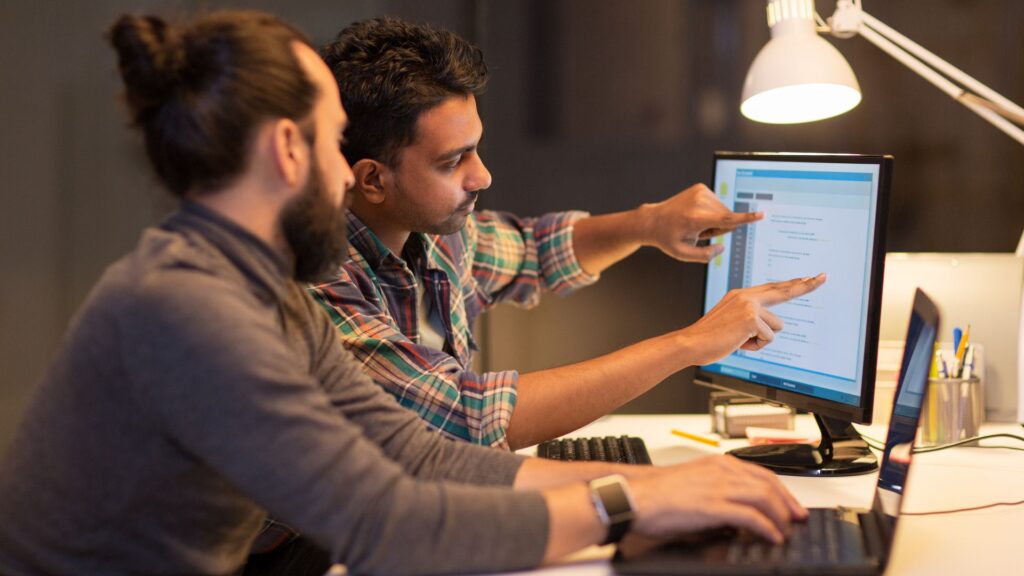 Two persons sitting by a computer at an office.