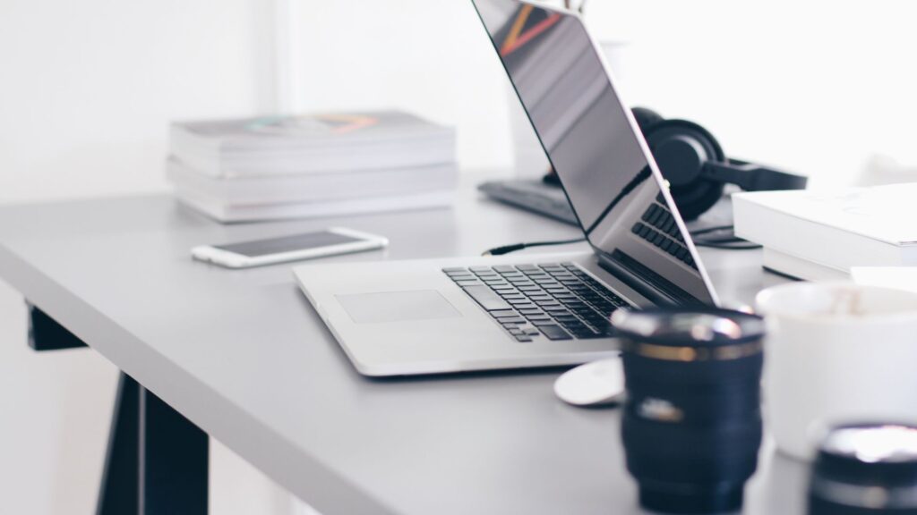 Laptop on office desk next to a smartphone, cup of coffee, and headphones.