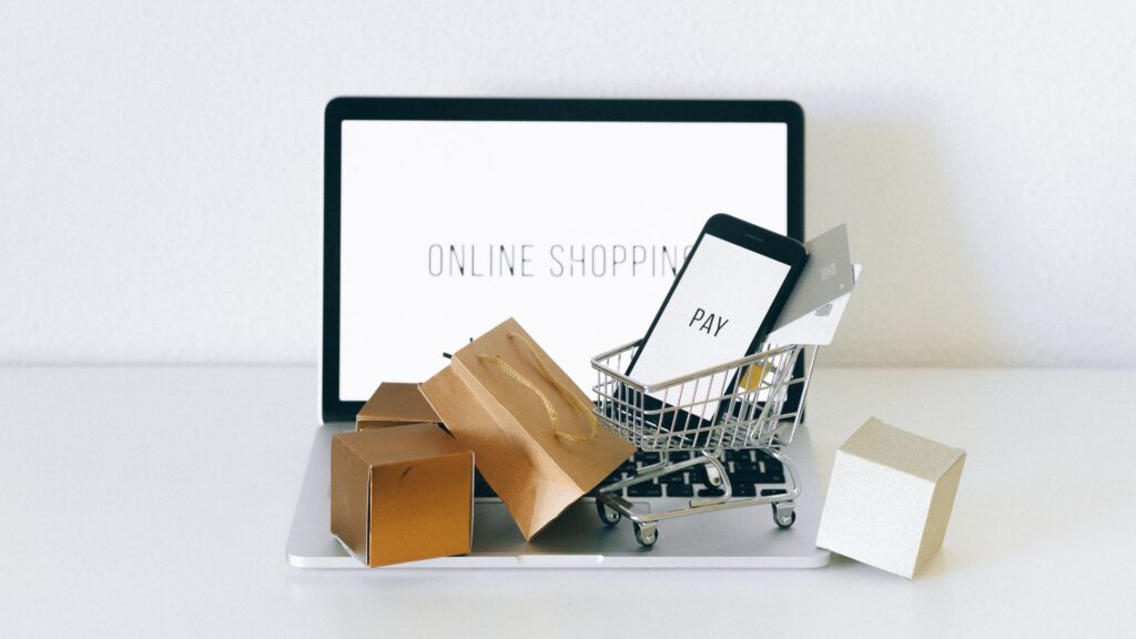 Laptop with miniature boxes and a miniature shopping cart on the keyboard.