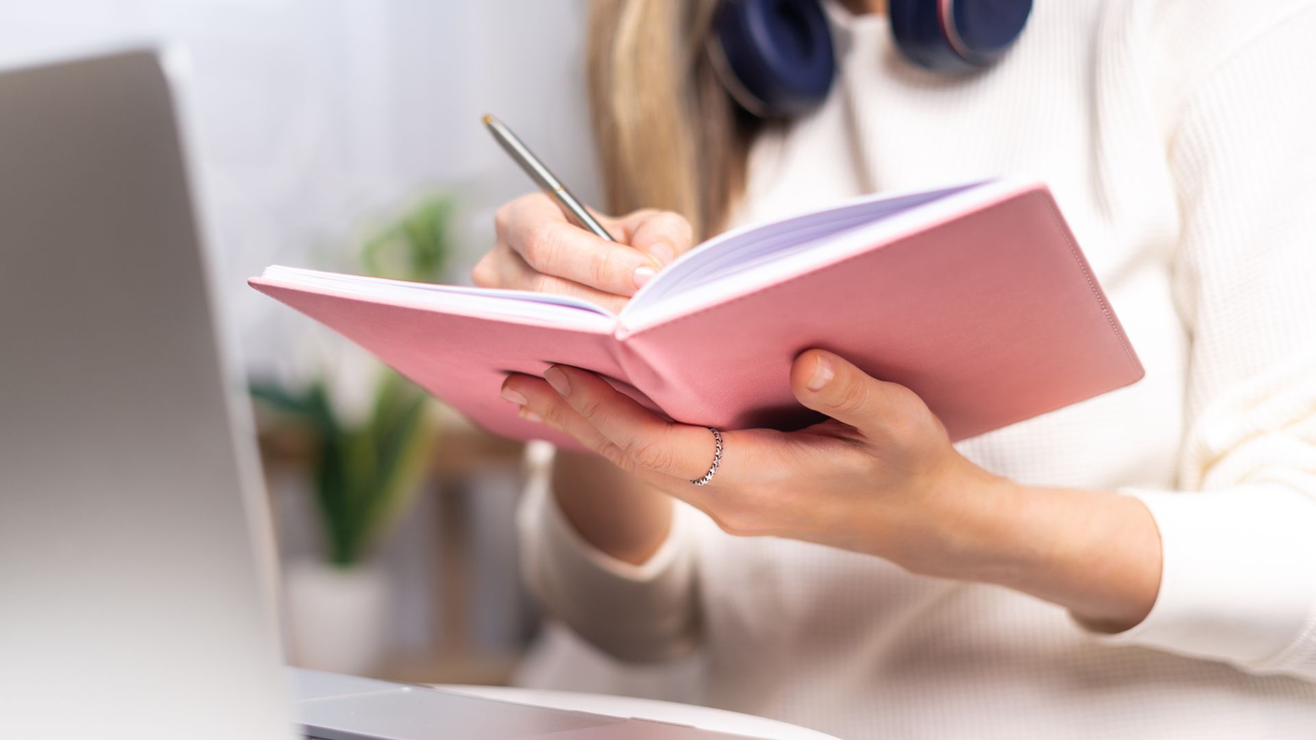 Woman sitting by laptop writing in a notebook.