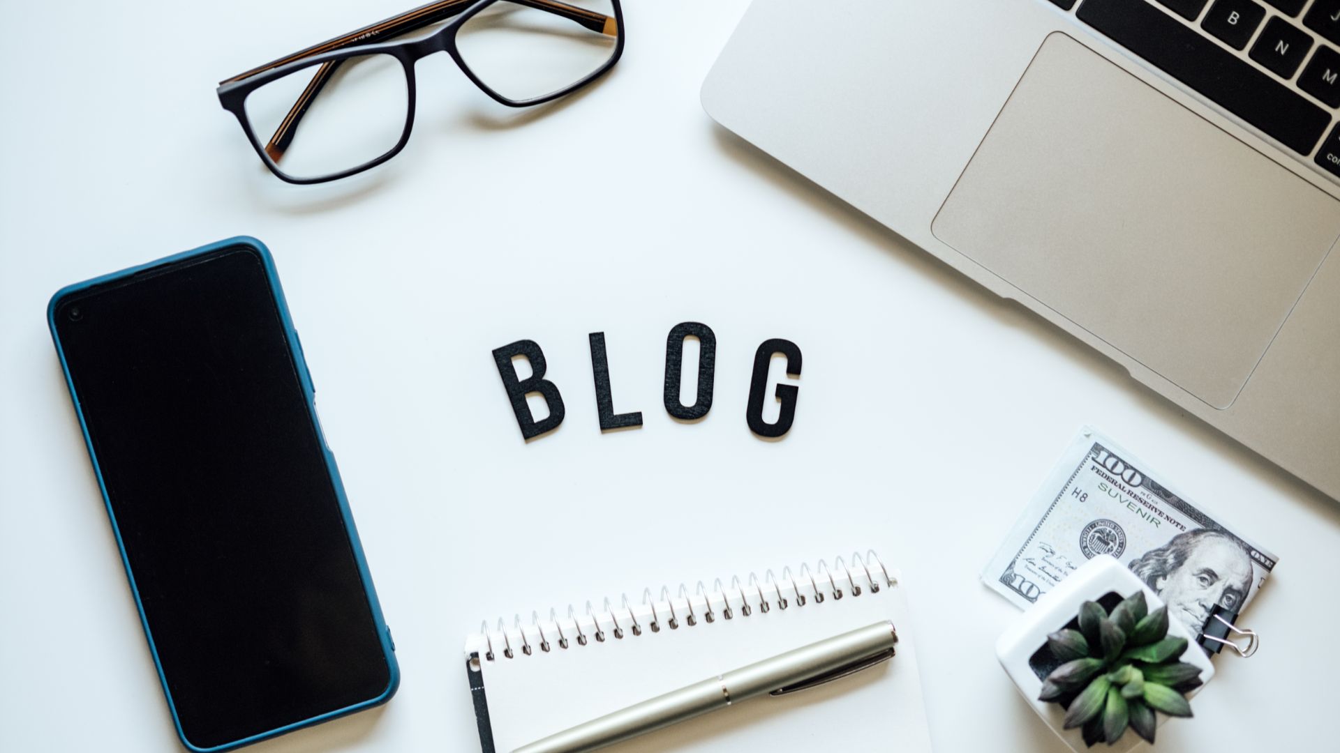 Desk with laptop, smartphone, glasses, notepad, and letters forming the word "BLOG".