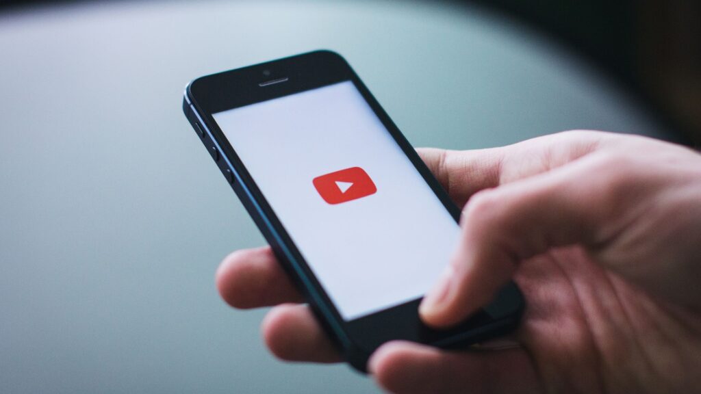 YouTube user holding a smartphone with a YouTube logo on the screen.